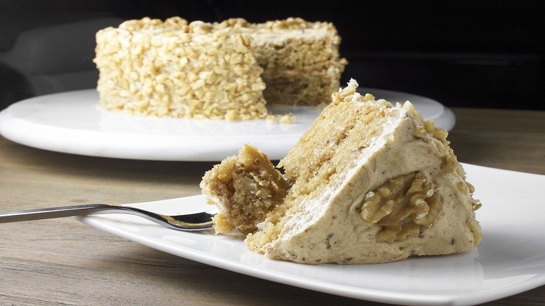 Image of a coffee and walnut cake slice with full cake in background